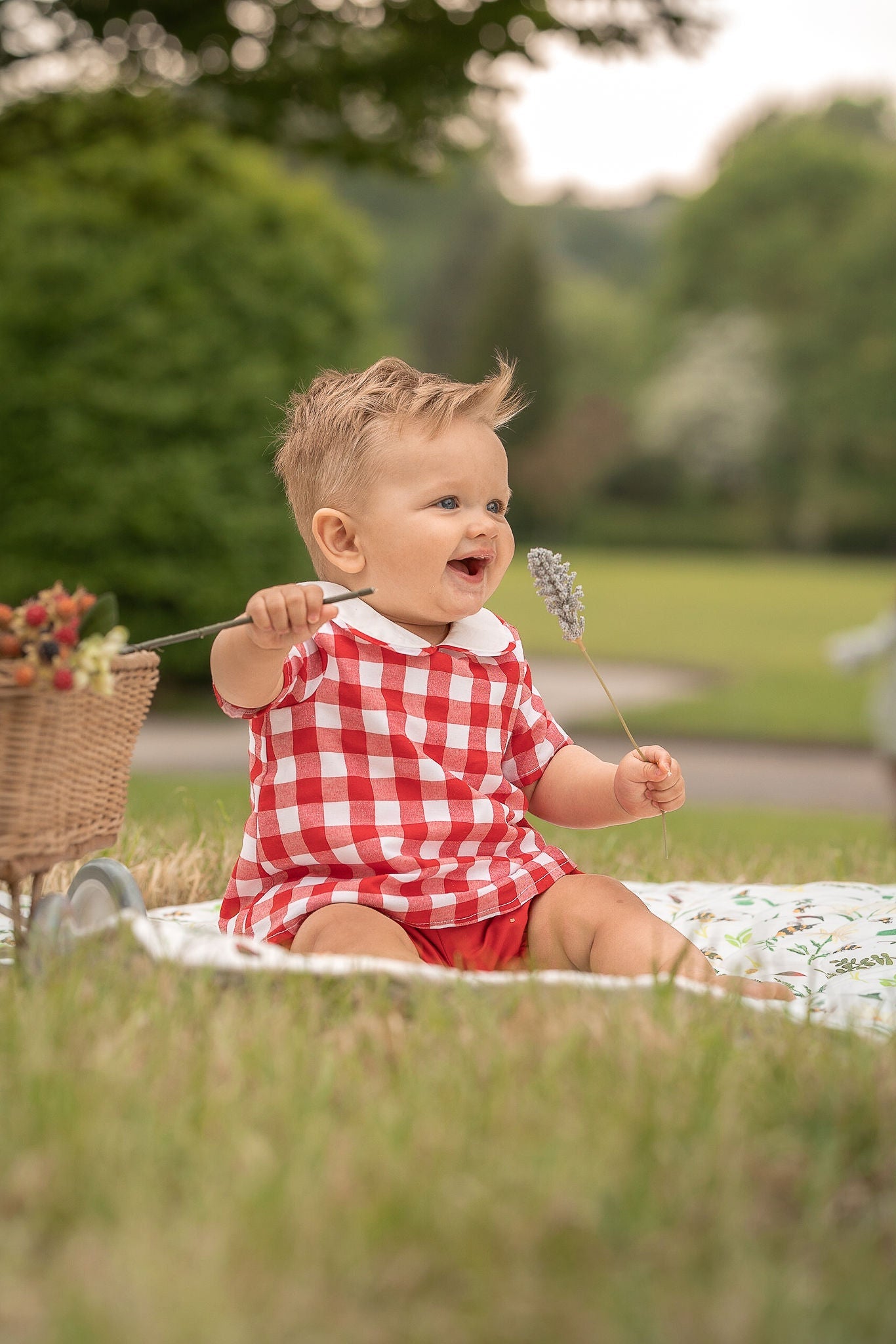 A baby boy wearing red gingham two piece set smiling to someone