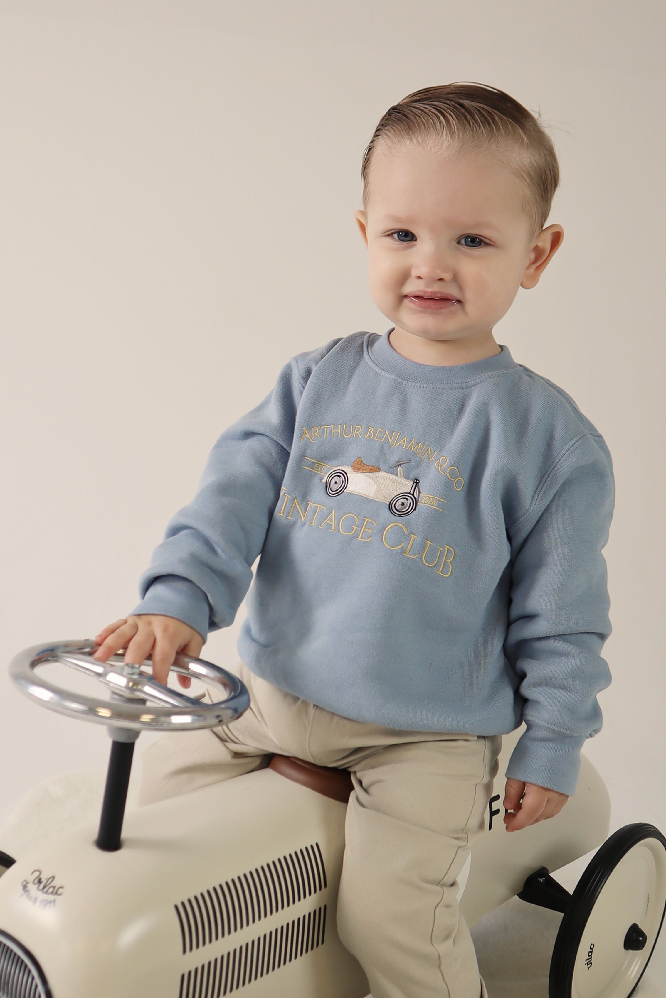 Blonde Boy sat on ride on car wearing blue sweater